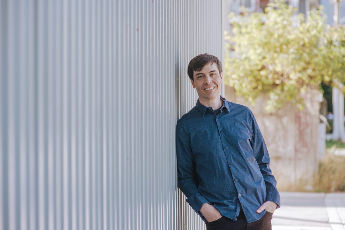 Chris Pettingill leaning against a corrugated metal wall in Squamish, hands in pockets, smiling